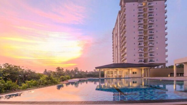 A high-rise hotel with a swimming pool and a covered area, surrounded by greenery.