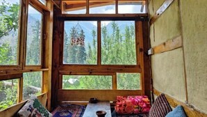 A cozy room with wooden walls and large windows, offering views of a forested mountain area. - Yalakhom (Sosan)