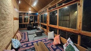 A cozy room with a wooden ceiling, large windows, a patterned rug, and a bench. - Yalakhom (Sosan)
