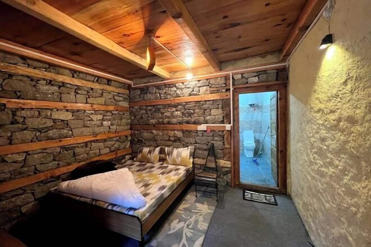 Une chambre avec un mur en pierre, des poutres en bois, un lit et une vue sur l’extérieur, visible à travers une porte vitrée.