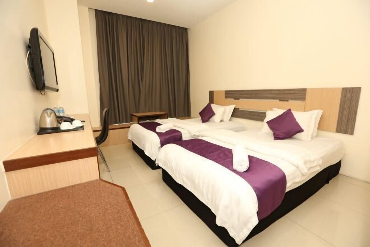 A hotel room with two beds, a desk with a kettle, a TV, and a large window with curtains.