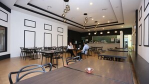 A modern dining area with multiple tables and chairs, a counter with a person serving, and a clean, minimalist design. - MY Fame Hotel (Rasah)