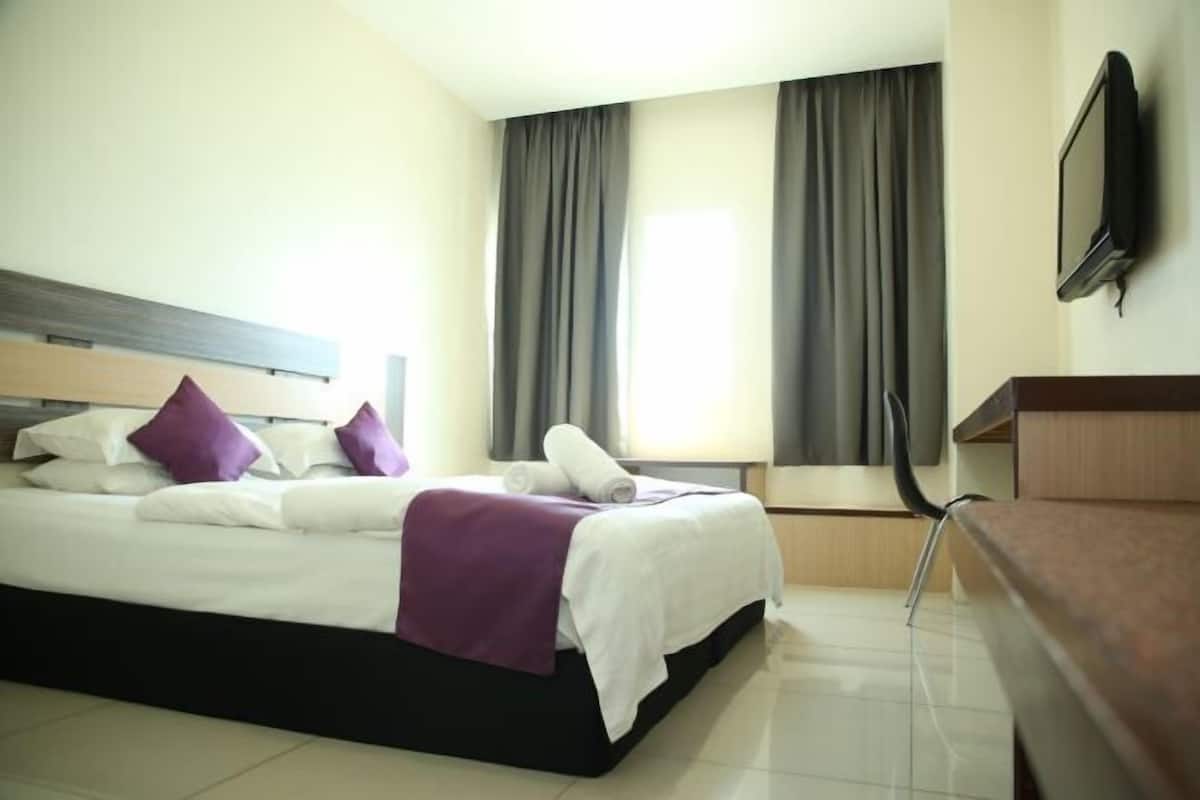 A hotel room with a bed, a desk, a chair, a TV, and curtains.