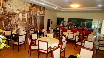 A dining area with round tables and chairs, a mural on the wall, and a bar area in the background.