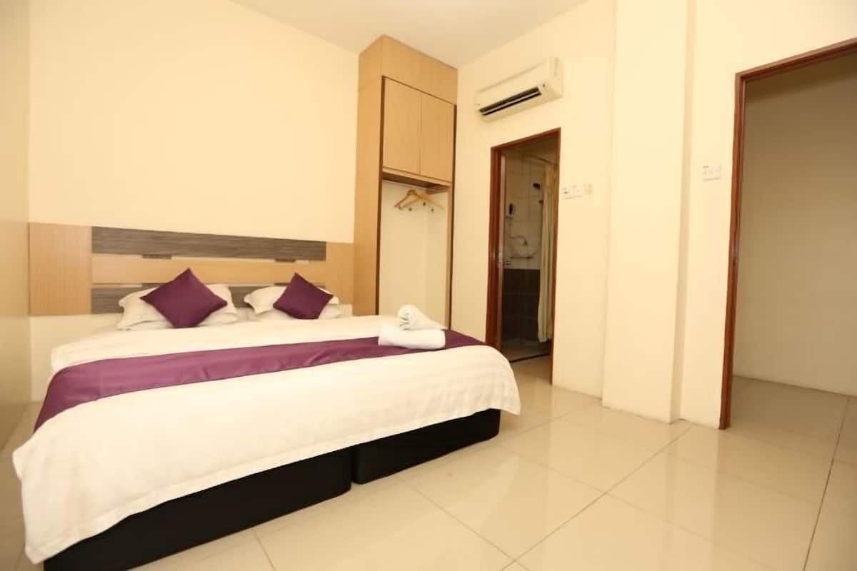 A neatly made bed with a headboard, a wooden wardrobe, and an air conditioning unit on the wall.