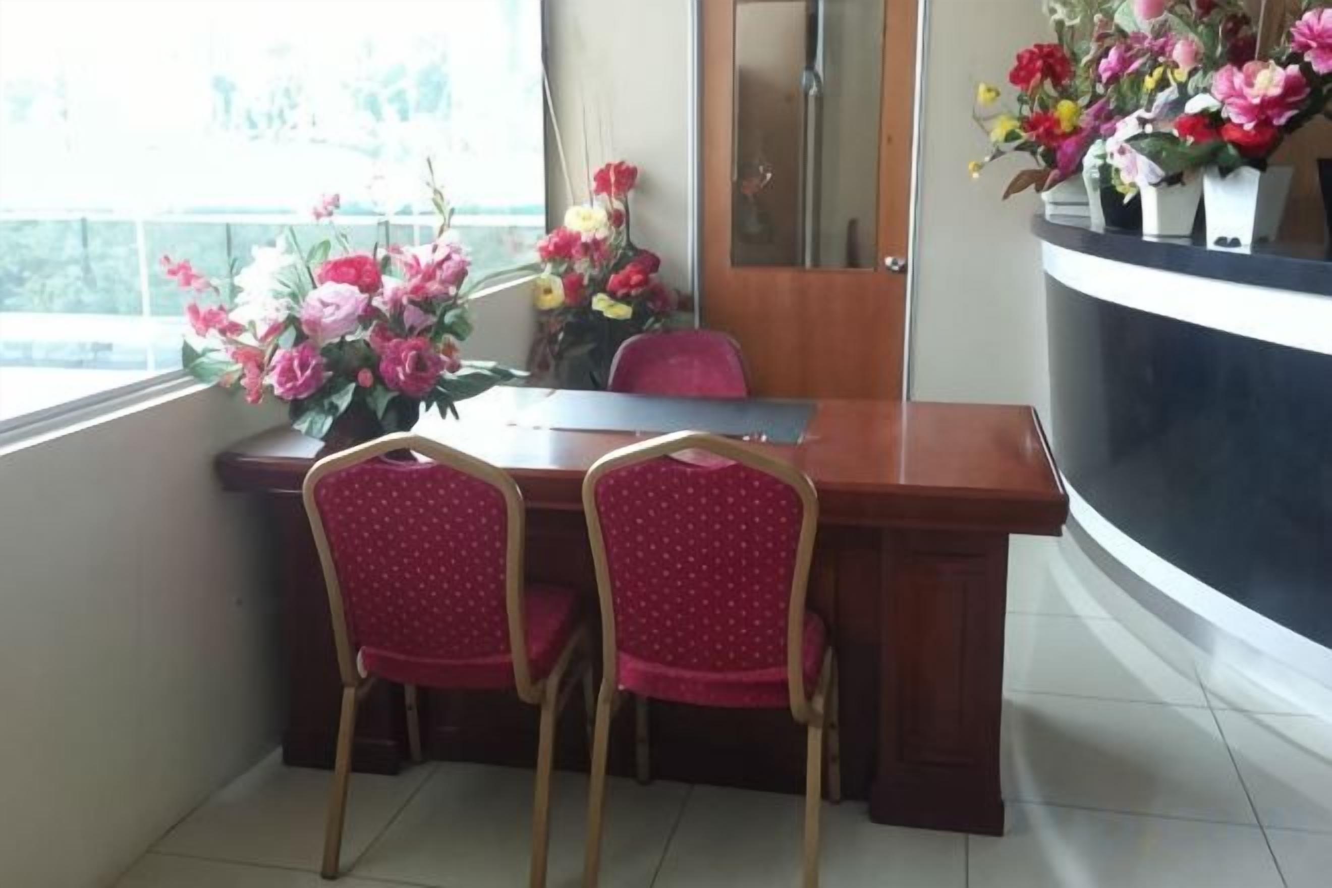 A dining area with a wooden table, two red chairs, and a vase of flowers.