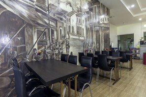 A restaurant with tables and chairs, a mural on the wall, and a kitchen area in the background. - MY Fame Hotel (Rasah)