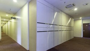 A hallway with a row of white lockers, carpeted floor, and a door at the end. - MY Fame Hotel (Rasah)