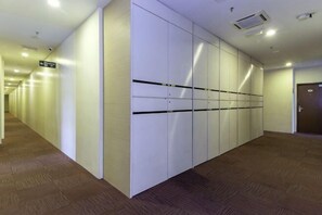 A hallway with a row of white lockers, carpeted floor, and a door at the end.