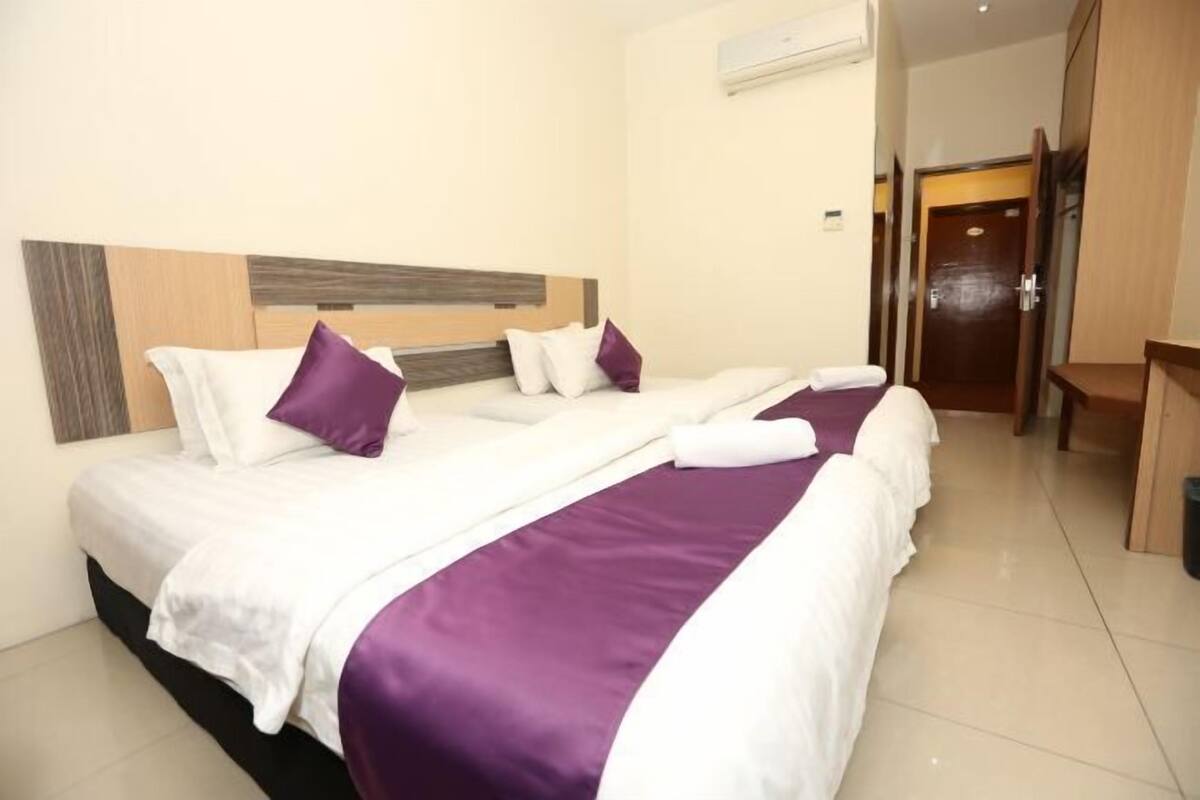 A hotel room with a large bed, a wooden headboard, and a door leading to a hallway.