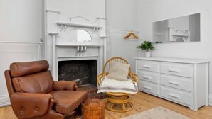 A room with a brown leather chair, a wicker chair, a white dresser, and a fireplace. - Wanderlust 3Br Cottage Grange Illuminate Adelaide 2024 (Grange)