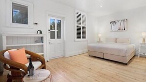 A bedroom with a bed, a chair, a small table, a door, and a window. - Wanderlust 3Br Cottage Grange Illuminate Adelaide 2024 (Grange)
