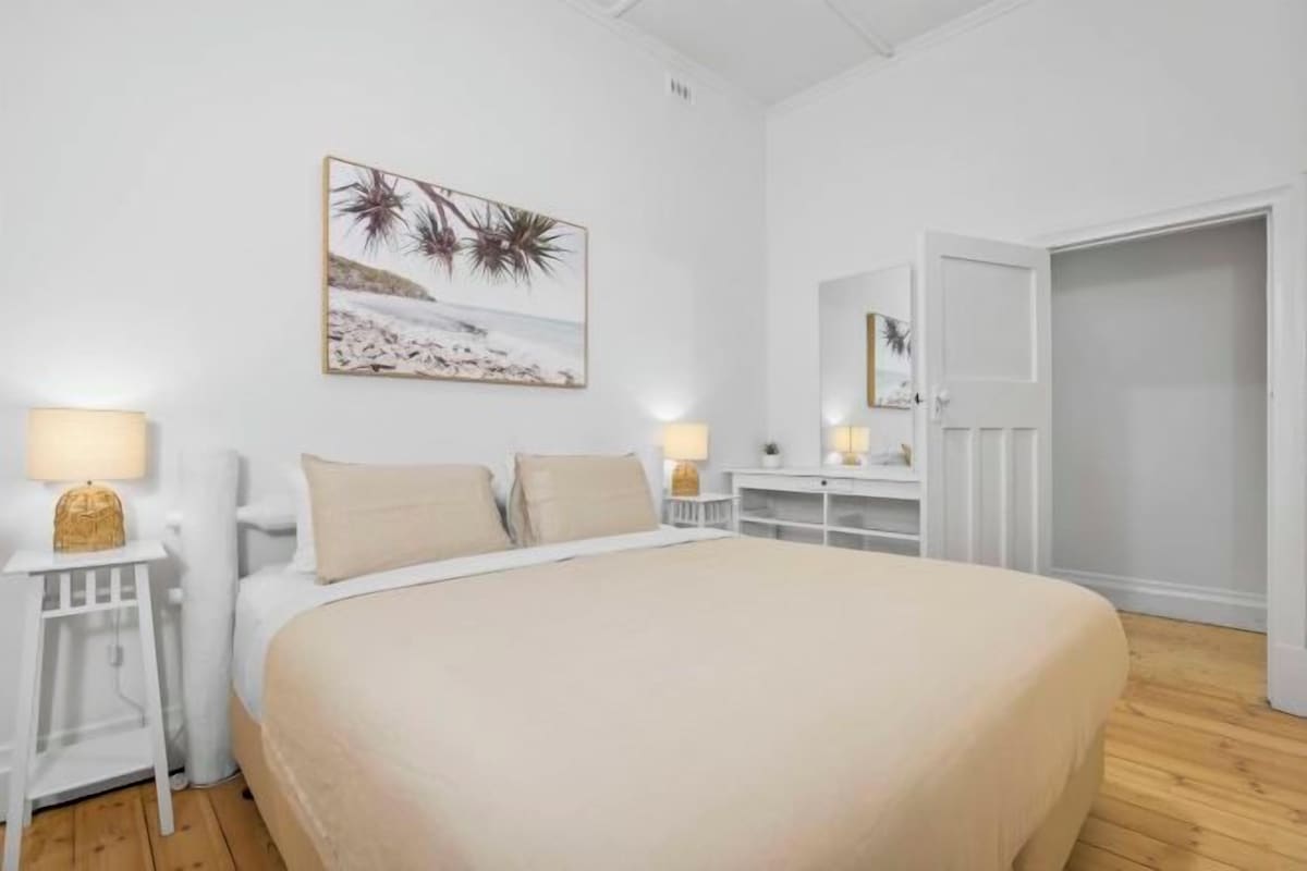 Un dormitorio con una cama grande, mesitas de noche con lámparas, un cuadro en la pared y un armario.