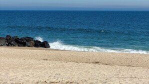 Ein Strand mit klarem, blauem Wasser, sandigem Ufer und dunklen Felsen im Hintergrund.