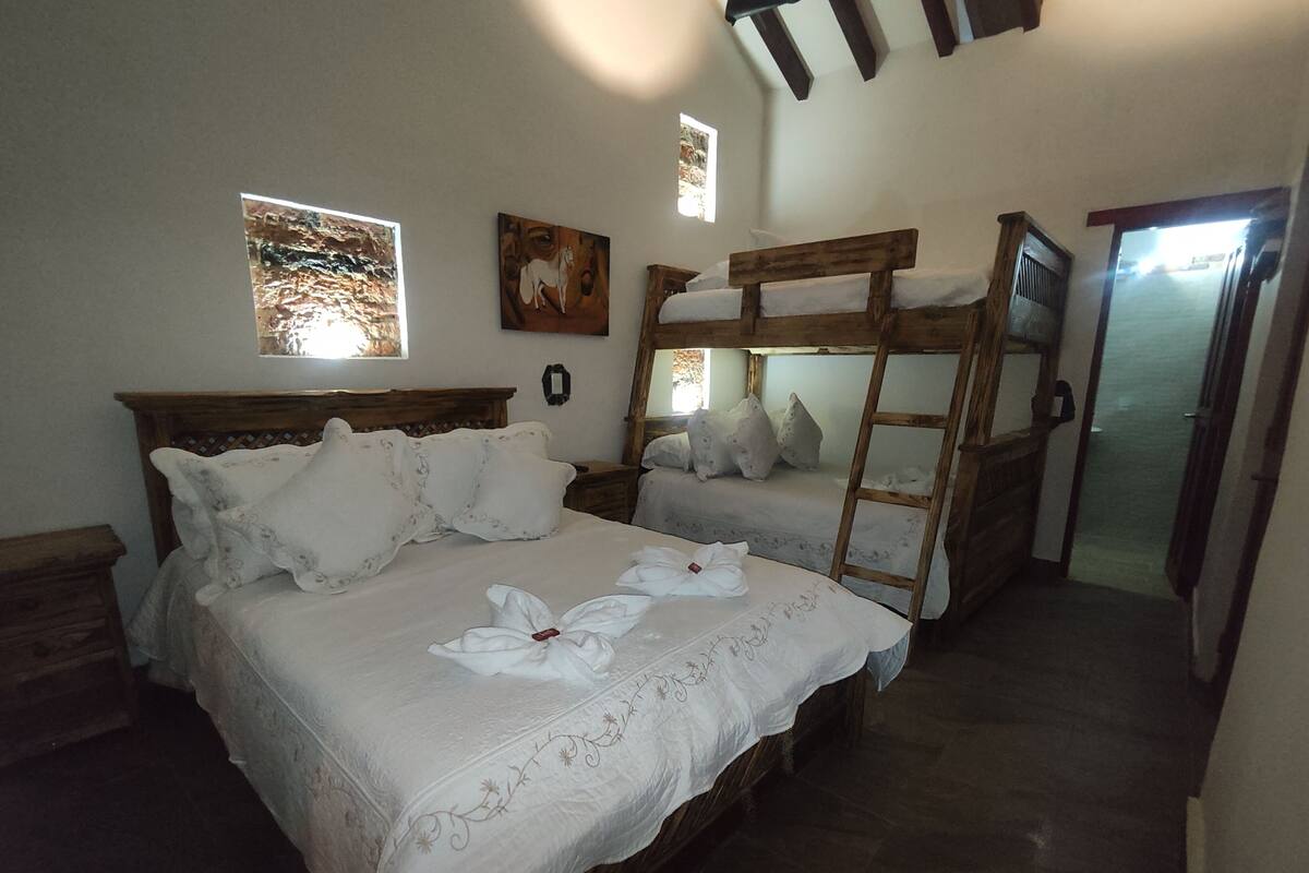 Ein Schlafzimmer mit zwei Etagenbetten, einer Holzleiter und einem Bett mit weißen Leinen und floralen Mustern.