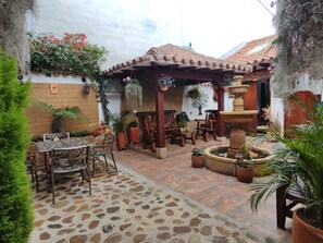A patio with stone flooring, wooden furniture, and potted plants. - Hostal la casita de toñito  (Villa de Leyva)