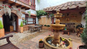 A courtyard with a stone fountain, outdoor seating, and potted plants. - Hostal la casita de toñito  (Villa de Leyva)