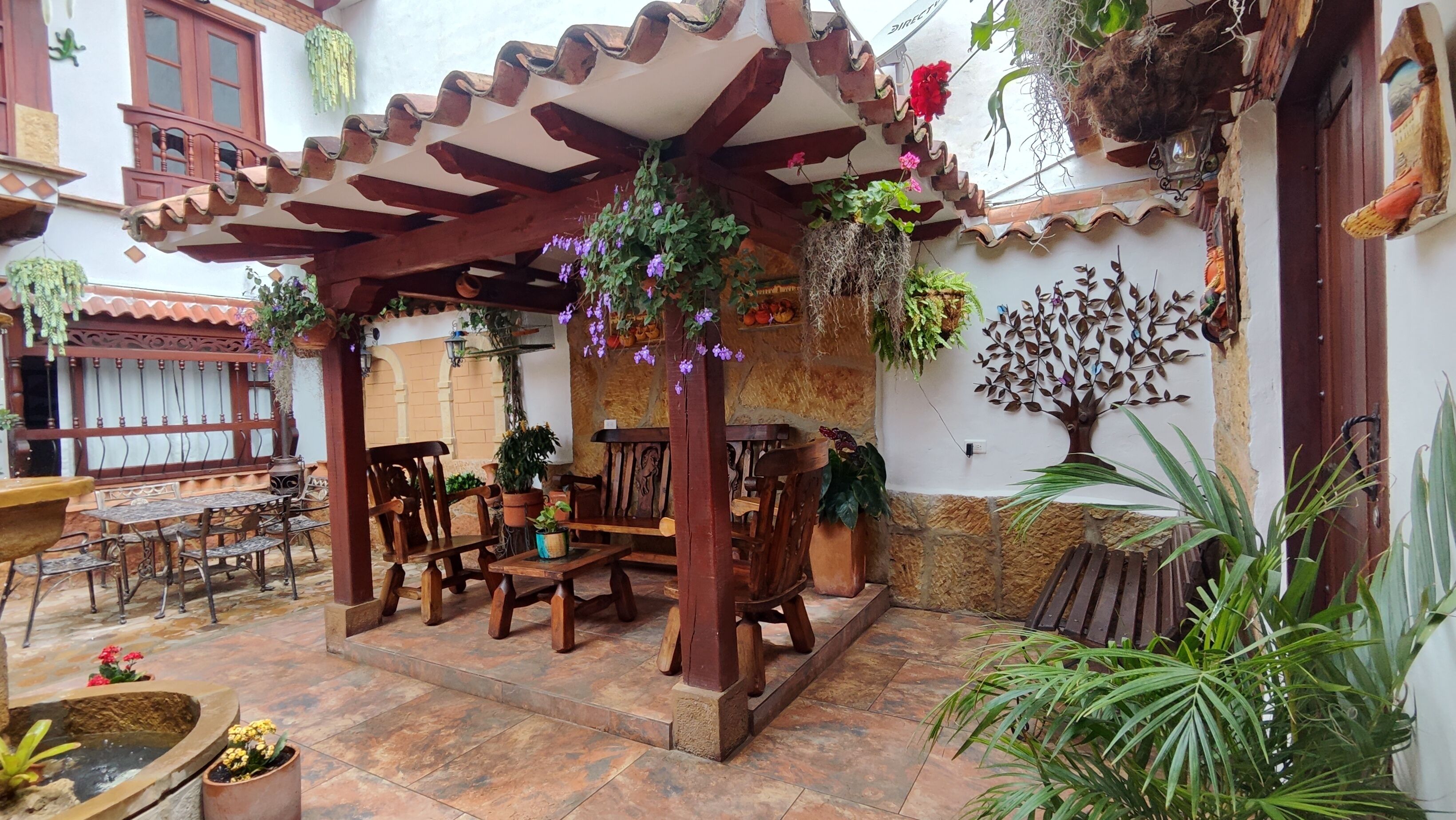 A covered patio area with wooden furniture, potted plants, and a decorative wall.