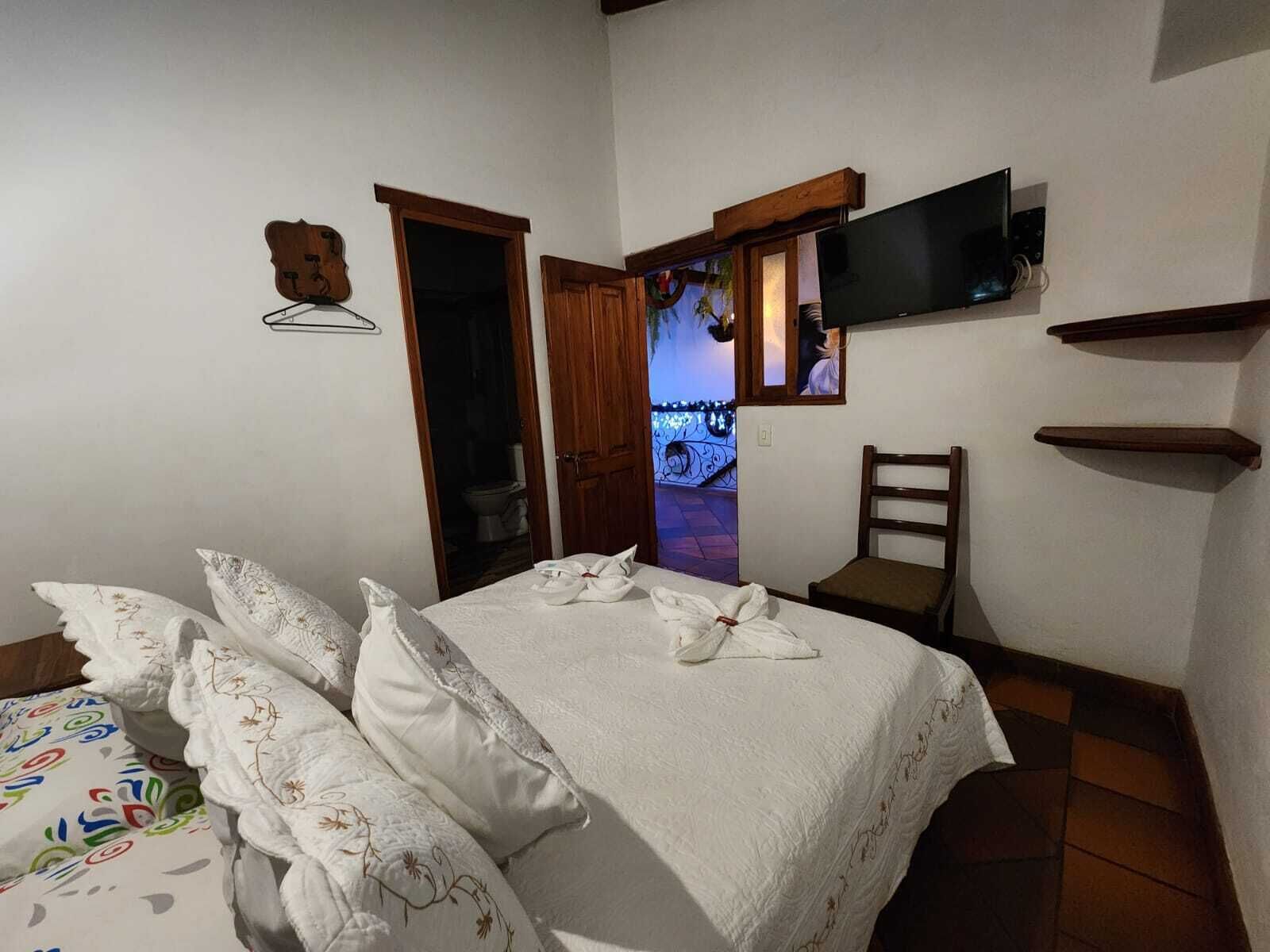 A bedroom with a bed, pillows, a chair, a TV, and a wooden shelf.