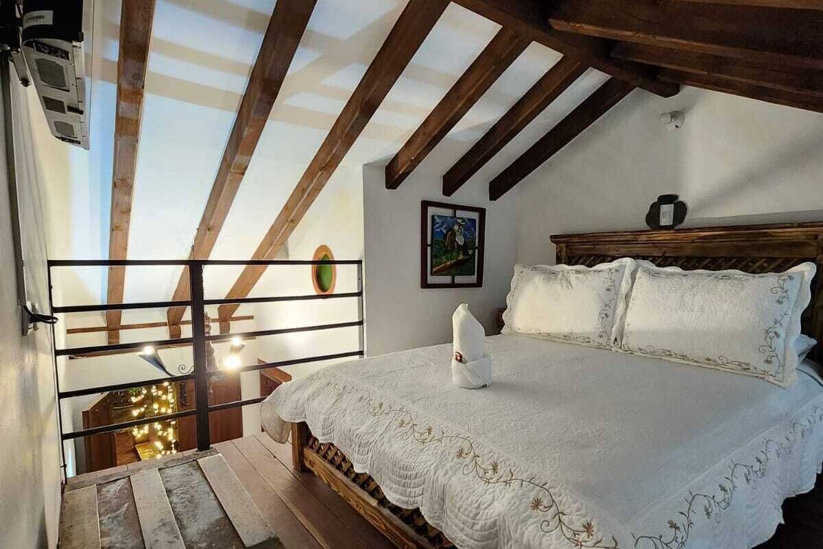 Ein Schlafzimmer mit Holzbalkendecke, einem Bett mit weißer Bettwäsche, einem kleinen Tisch und einem Bild an der Wand.