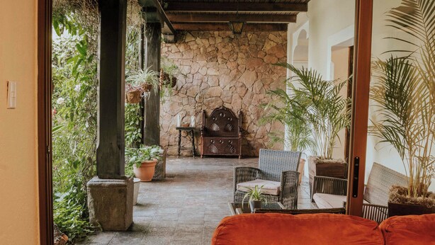 A stone-walled patio with a wooden bench, potted plants, and a wicker chair. - Amazing Historic  Spanish House with AC, WIFI Cable and an amazing Courtyard.  (Antigua Guatemala)