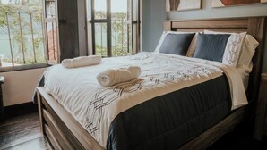 A neatly made bed with a geometric patterned bedspread, a wooden headboard, and a view of the outdoors through a window. - Amazing Historic  Spanish House with AC, WIFI Cable and an amazing Courtyard.  (Antigua Guatemala)