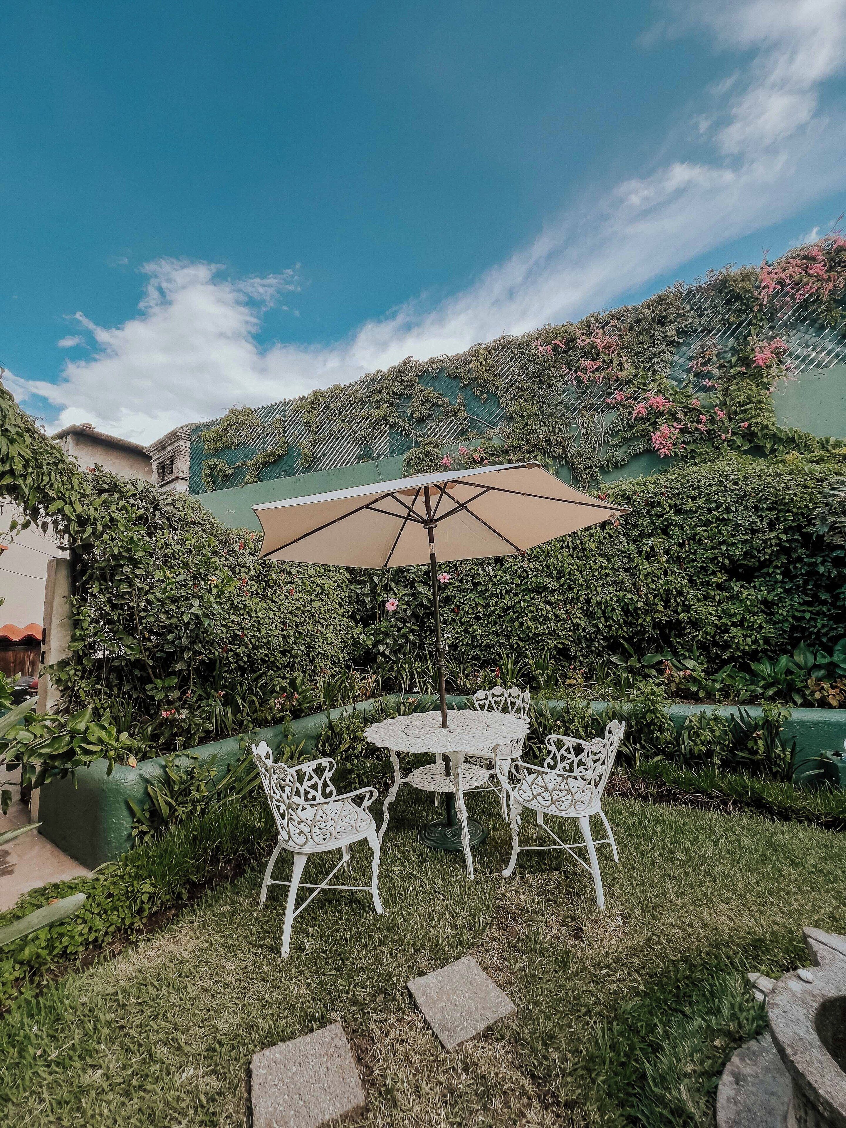 An outdoor seating area with a round table and four chairs, an umbrella, and a green wall with climbing plants.