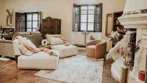 A living room with a sofa, armchair, and ottoman, a fireplace, and a large window with curtains. - Amazing Historic  Spanish House with AC, WIFI Cable and an amazing Courtyard.  (Antigua Guatemala)
