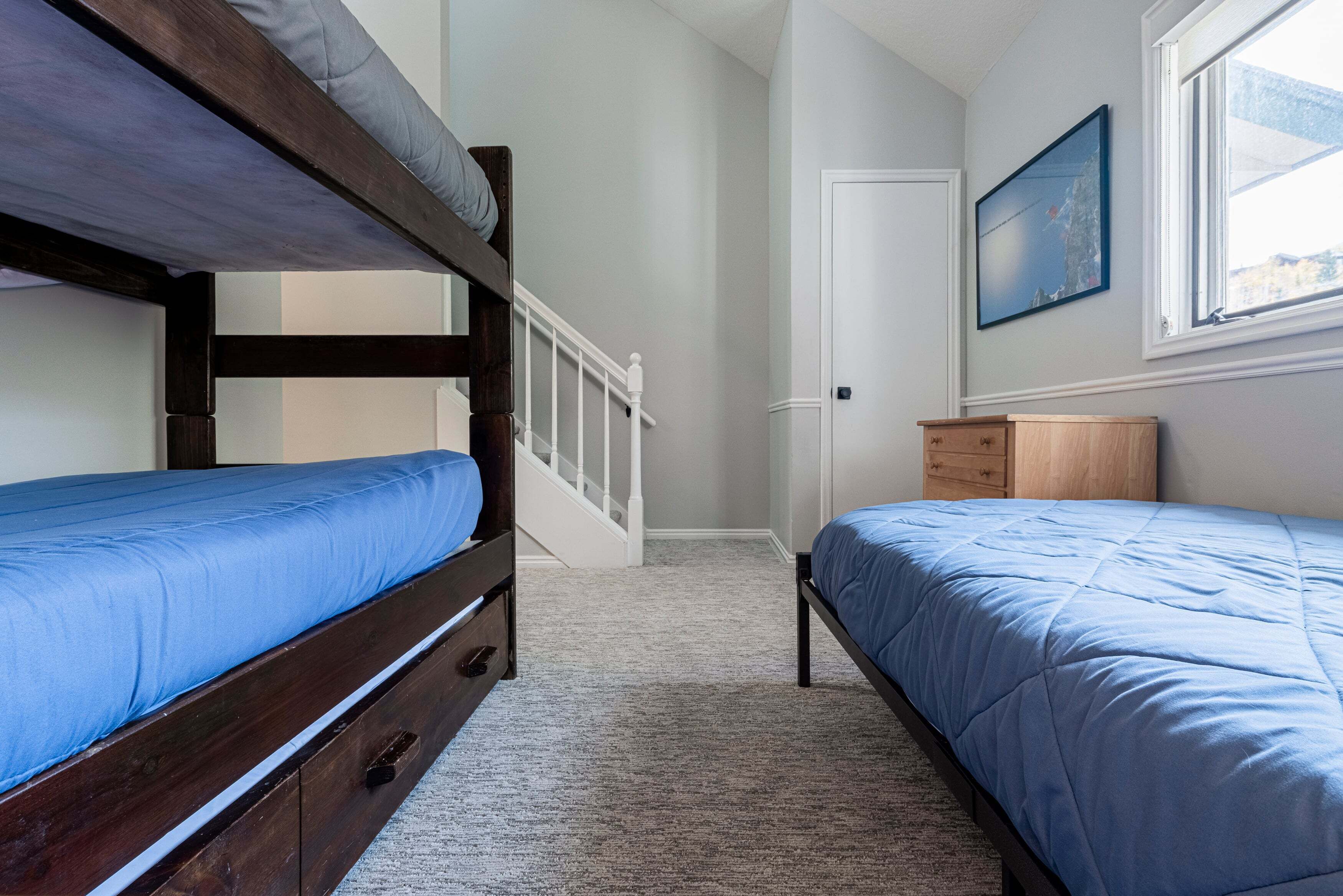 A bedroom with two bunk beds, a wooden dresser, a door, and a window with a painting.