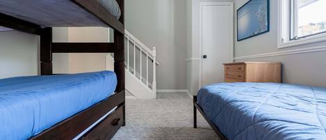 A bedroom with two bunk beds, a wooden dresser, a door, and a window with a painting.