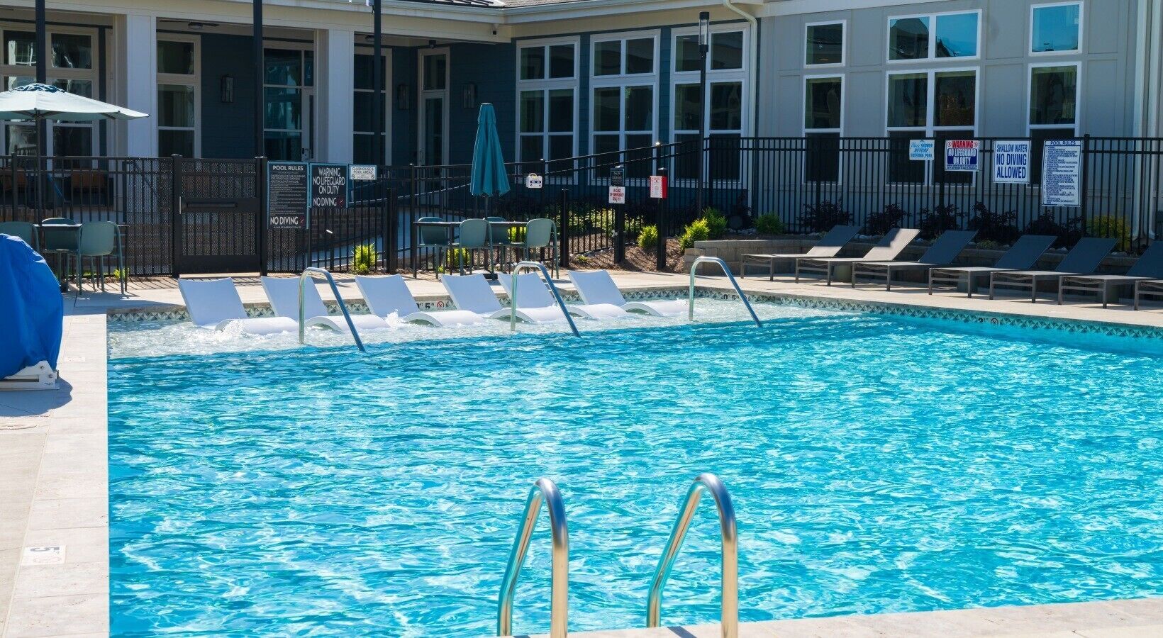 Une piscine avec des chaises longues, une tour de surveillance pour les sauveteurs et, au fond, un bâtiment doté de grandes fenêtres.
