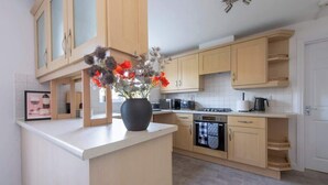 A modern kitchen with wooden cabinets, a central island with a vase of flowers, and a built-in oven. - Modern 5BR * Game Room * Free Parking * Sleeps 10 (Hornchurch)
