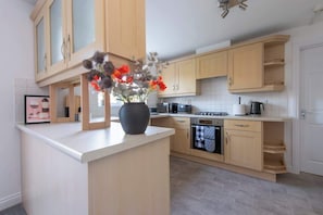A modern kitchen with wooden cabinets, a central island with a vase of flowers, and a built-in oven.