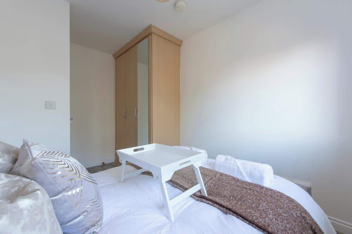Een slaapkamer met een bed, een witte nachtkastje, een kledingkast en een deur.