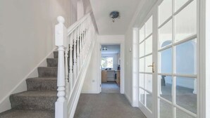 A staircase leading to a second floor, a hallway with a door, and a glimpse of a kitchen area. - Modern 5BR * Game Room * Free Parking * Sleeps 10 (Hornchurch)