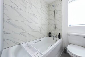 Et badeværelse med badekar, toilet og bruser.