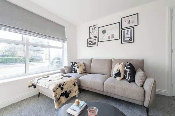 A living room with a sofa, a coffee table, a window with blinds, and wall art.