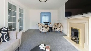 A living room with a sofa, two armchairs, a fireplace, a television, and a door with glass panels. - Modern 5BR * Game Room * Free Parking * Sleeps 10 (Hornchurch)