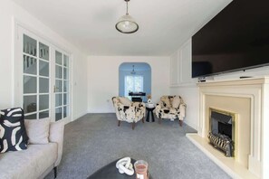 A living room with a sofa, two armchairs, a fireplace, a television, and a door with glass panels.
