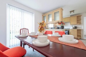 A dining area with a table set for four, a kitchen in the background, and a window with blinds.