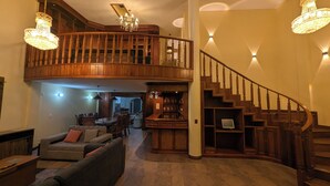 A spacious living area with a high ceiling, a wooden staircase, and a bar area. - Luxurious house near the airport - Tumbaco center (Quito)