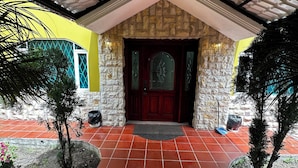 A covered entrance with a red-tiled floor, stone walls, and a dark wooden door with glass panels. - Luxurious house near the airport - Tumbaco center (Quito)
