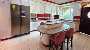 A kitchen with white cabinets, a granite countertop island with bar stools, a refrigerator, and a window with a view. - Luxurious house near the airport - Tumbaco center (Quito)