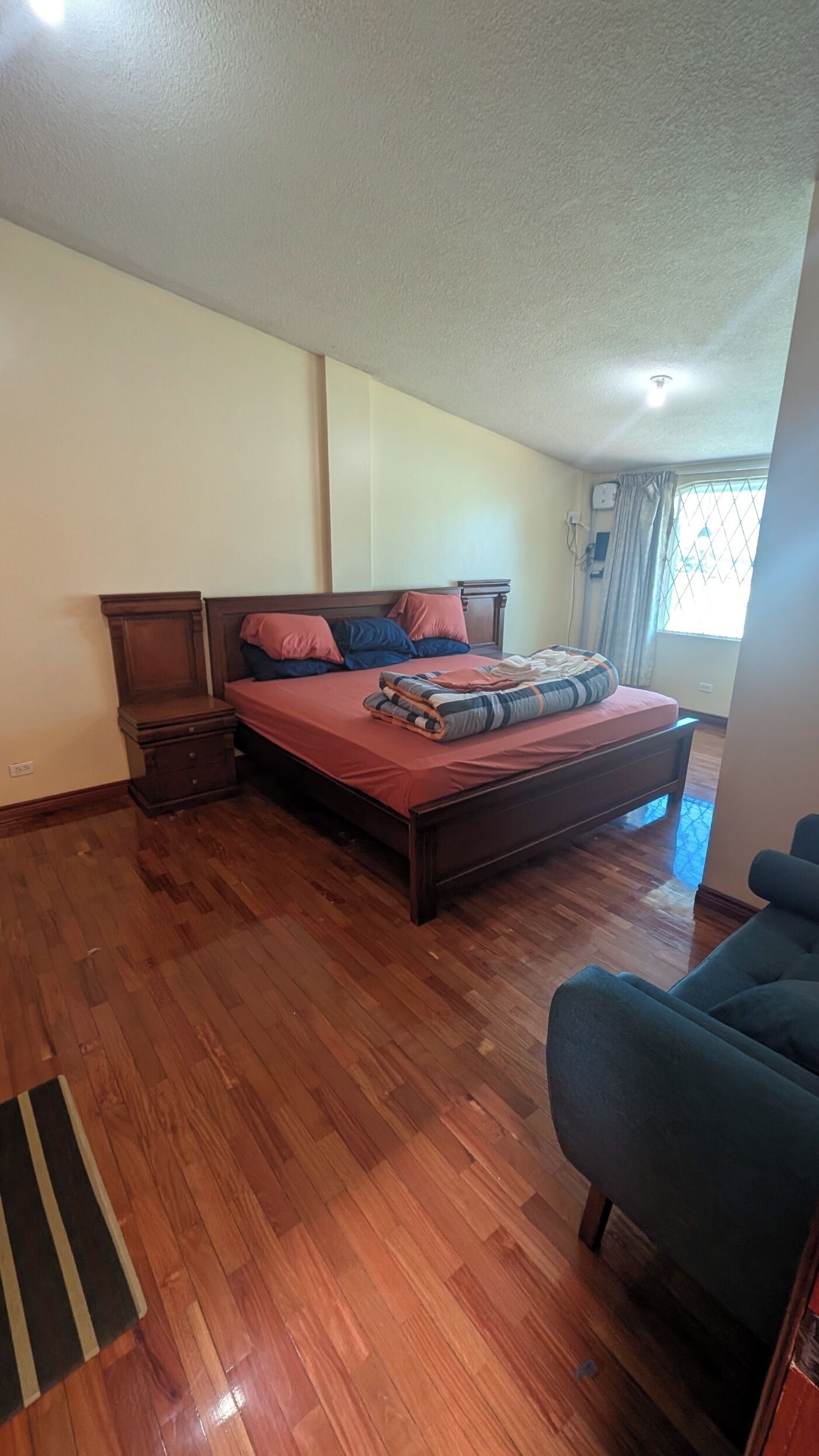A bedroom with a wooden bed, a nightstand, a dresser, and a window with curtains.