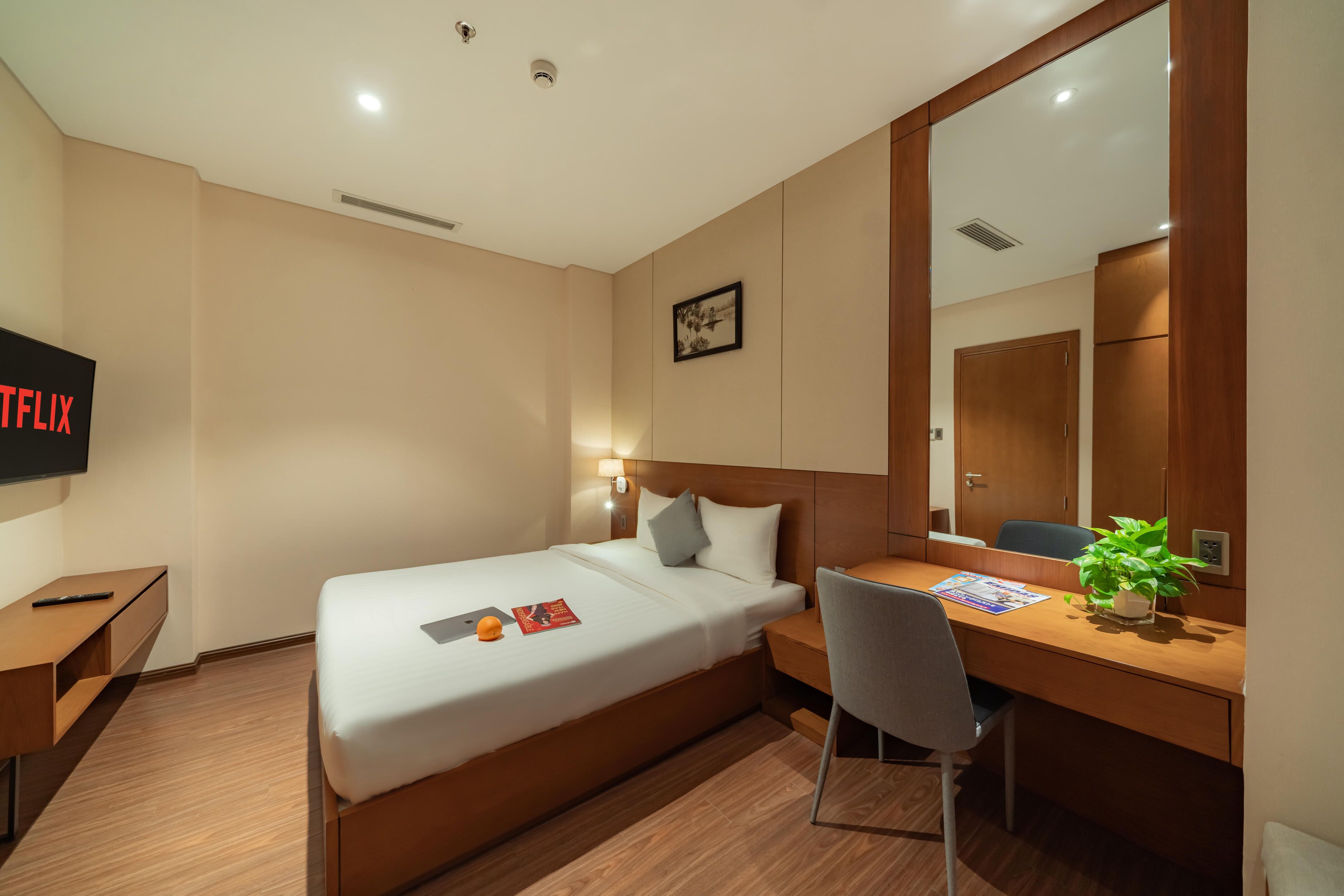 A hotel room with a bed, desk, chair, and a TV mounted on the wall.