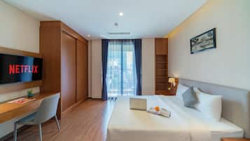 A hotel room with a bed, a desk with a laptop, a TV displaying 'NETFLIX', and a window with curtains.