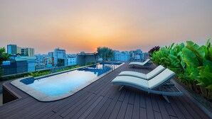 A rooftop pool area with lounge chairs and a view of the city skyline at sunset. - DHTS Business Hotel & Apartment (Ho Chi Minh City)