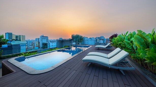 A rooftop pool area with lounge chairs and a view of the city skyline at sunset. - DHTS Business Hotel & Apartment (Ho Chi Minh City)