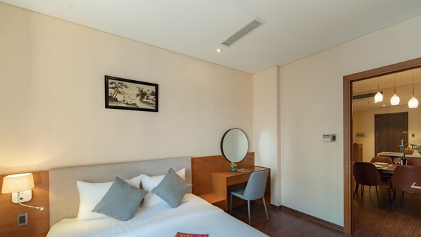 A hotel room with a bed, desk, chair, and a dining area visible through an open door. - DHTS Business Hotel & Apartment (Ho Chi Minh City)