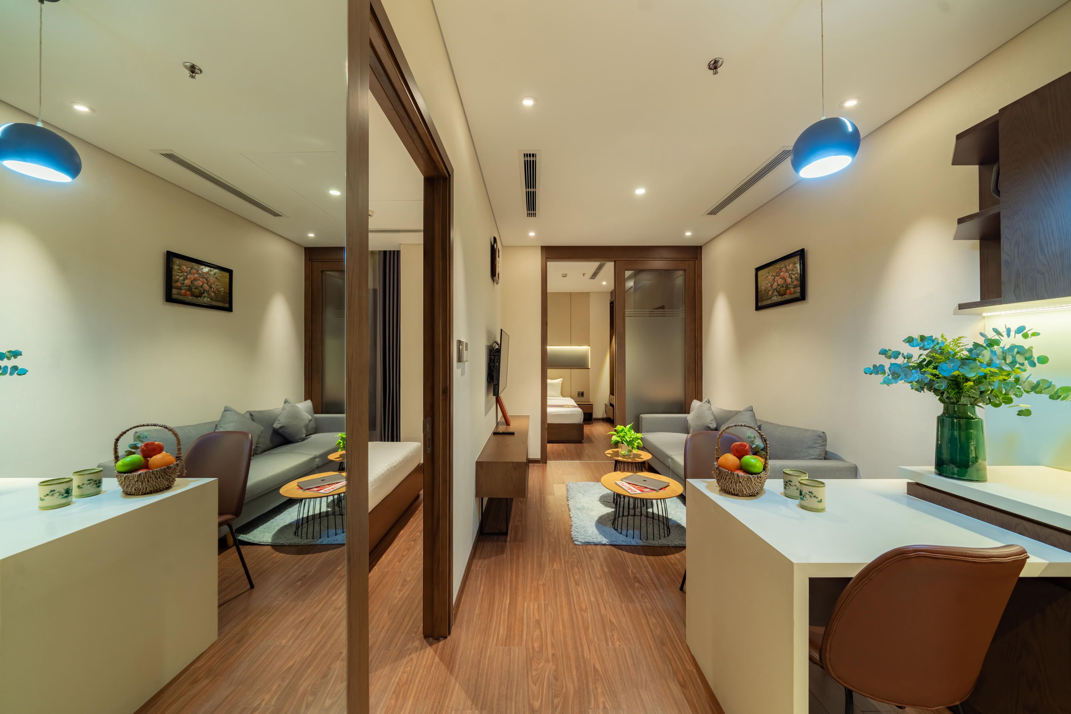 A modern hotel room with a dining area, a sofa, a coffee table, and a vase with flowers.